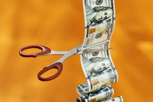 Stack of money being cut by scissors.